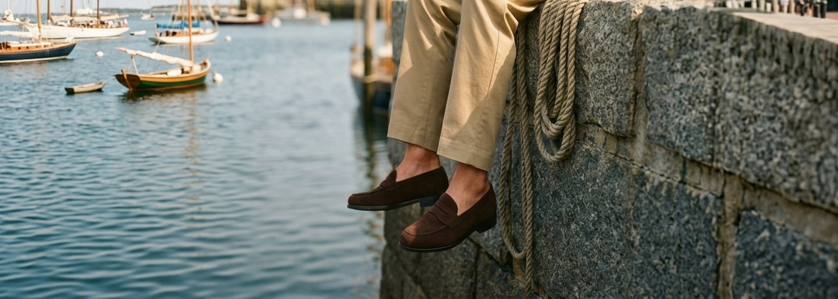 Man sitting on dock wearing chinos and brown Italian suede penny loafer dress shoes