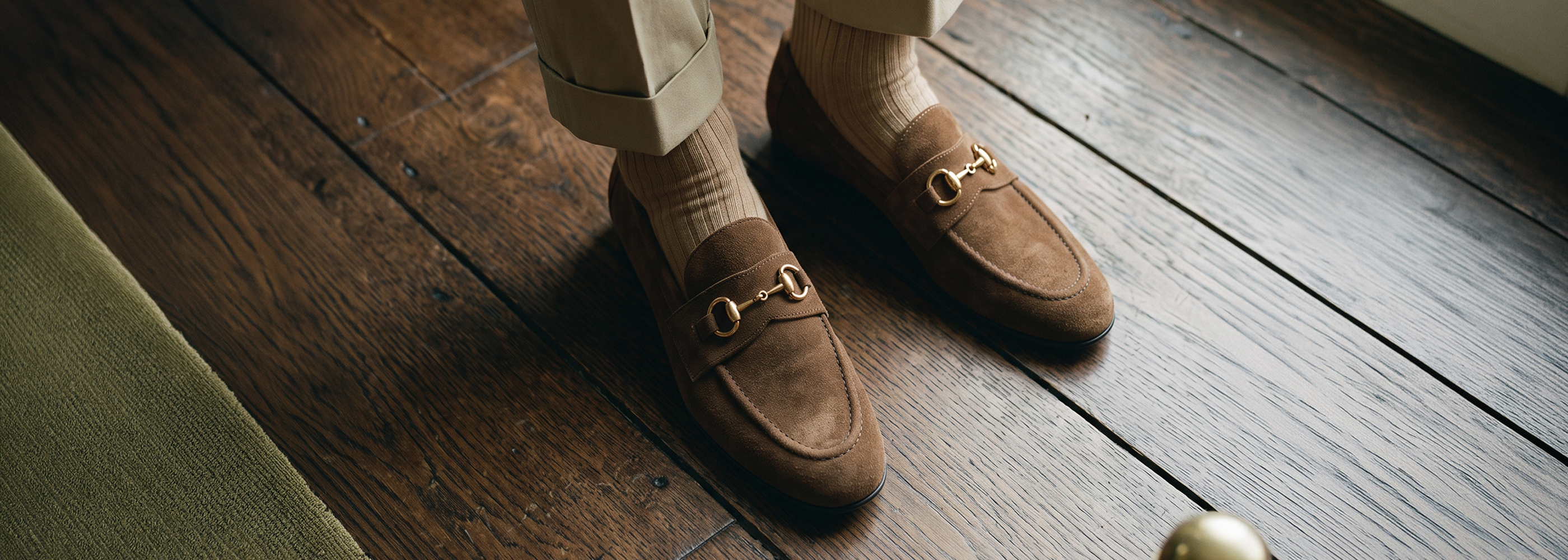 Man standing on wooden floor wearing men's brown Italian leather suede bit loafers with khakis and beige socks.