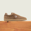 Men's golden brown European suede lace-up sneaker with beige rubber sole on a wooden platform.