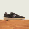 Men's dark brown European suede lace-up sneaker with beige rubber sole on a wooden platform.