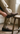 A person wearing men's brown European leather suede penny loafers, cream ribbed socks, and khaki trousers, sitting on a wooden stool in a room with a rustic wood floor and white wall.